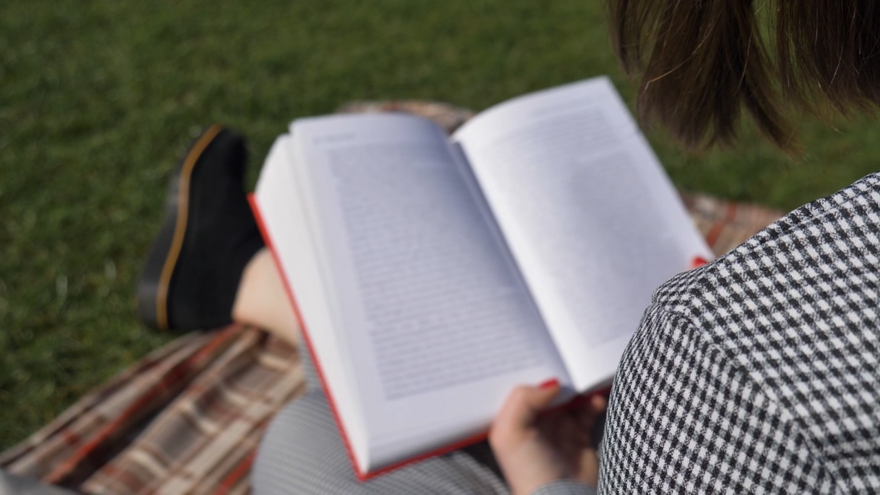 Sliding Over the Shoulder Shot of Young Woman Reading Book In Park